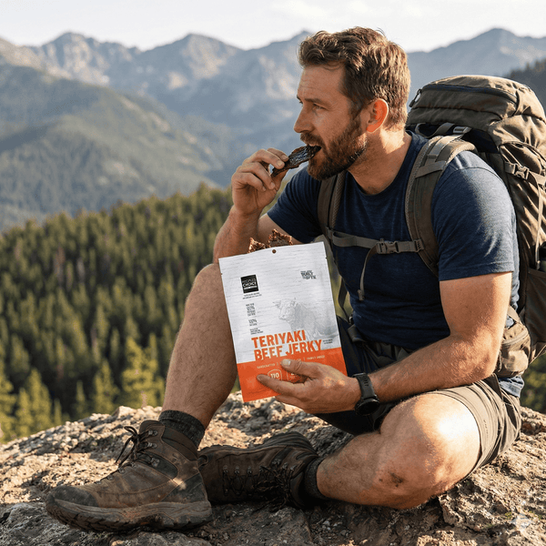 Man in outdoor setting eating Teriyaki Beef Jerky with mountains in the background