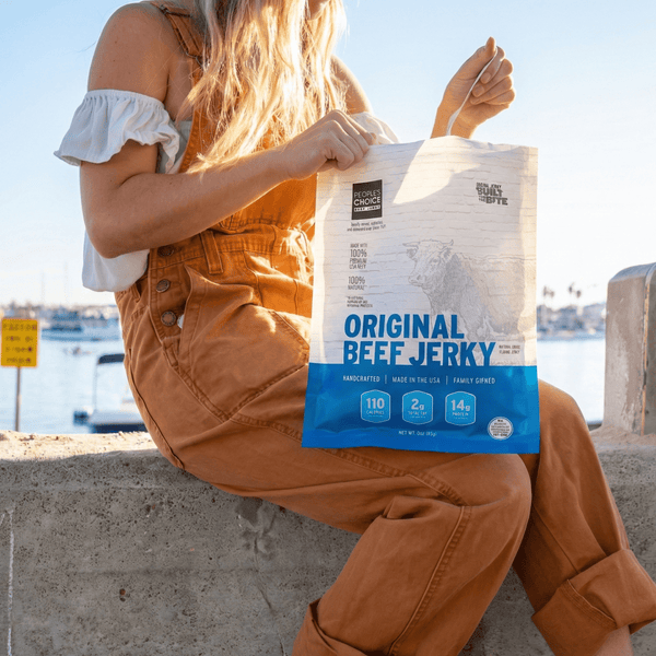 Person holding a bag of Original Beef Jerky by a waterfront.