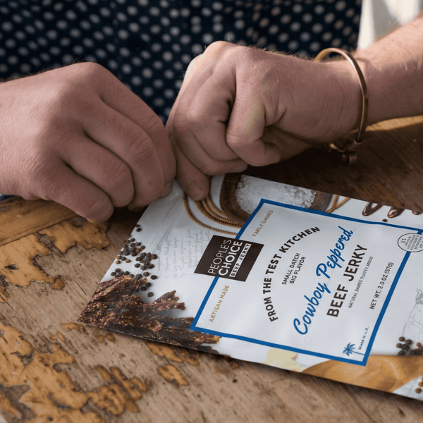 Person opening a package of 'Cowboy Peppered Beef Jerky' with a rustic background