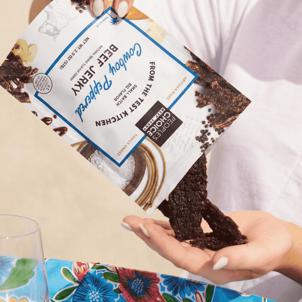 Person holding a package of Cowboy Peppered beef jerky with a visible brand label on a colorful tablecloth.
