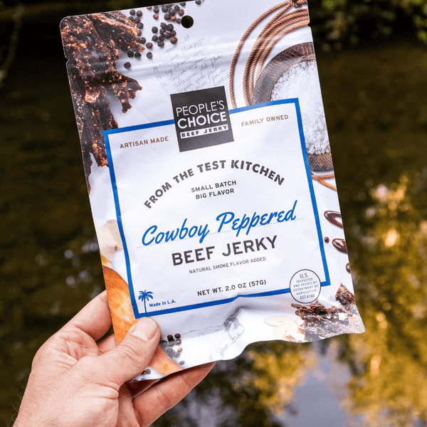 Hand holding a package of People's Choice Cowboy Peppered Beef Jerky with a natural background.