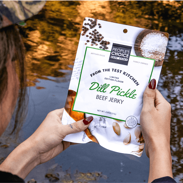 Person holding a package of Dill Pickle Beef Jerky by People's Choice in front of a body of water.