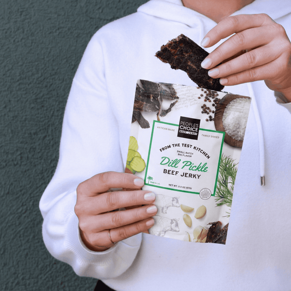 Person holding a package of Dill Pickle Beef Jerky against a gray background