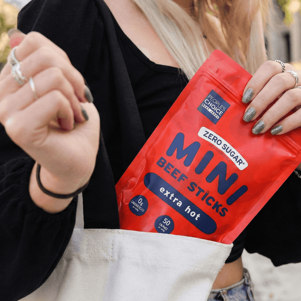 Person holding a red package of beef sticks with visible branding on a street background