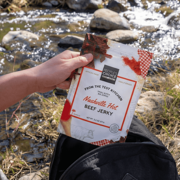 Person holding a package of beef jerky near a stream with rocks and grass.