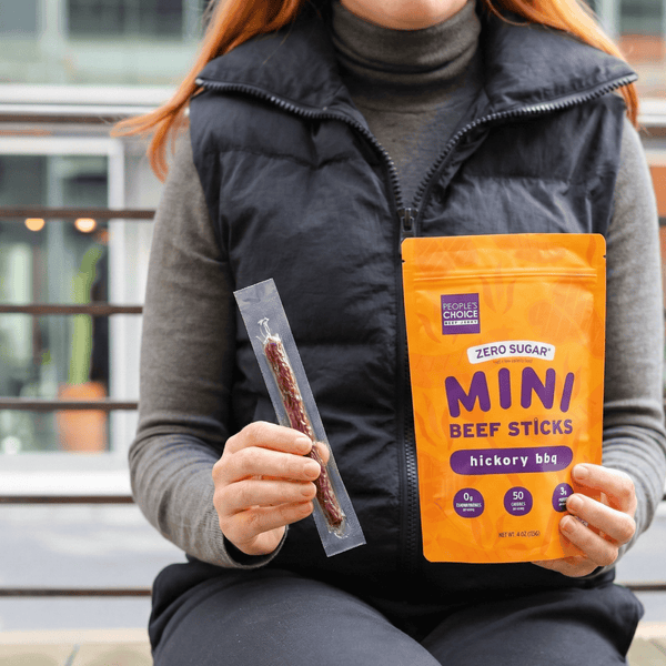 Person holding a package of People's Choice Mini Beef Sticks in a city setting