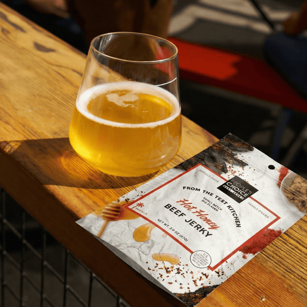 Glass of beer next to a package of beef jerky on a wooden surface