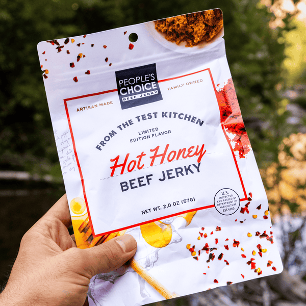 Hand holding a package of People's Choice Hot Honey Beef Jerky with a natural background.