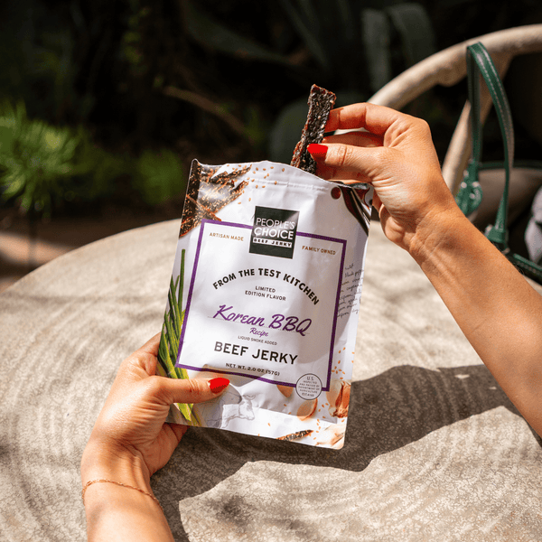 Someone pulling a piece of korean bbq beef jerky out of a bag while at a table