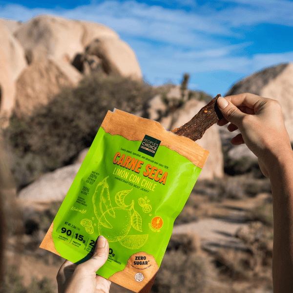Person holding a package of Carne Seca Limon Con Chile beef jerky in a desert setting