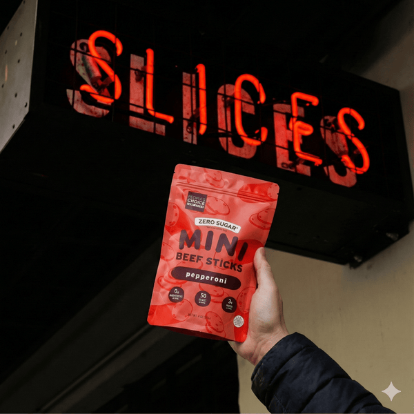 Hand holding a red package of Mini Beef Sticks in front of a neon sign with the word 'SLICES'.