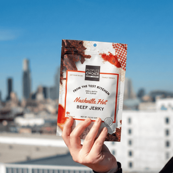 Hand holding a package of Nashville Hot Beef Jerky with a city skyline in the background