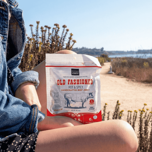 Woman holding a bag of Old Fashioned Hot & Spicy beef jerky outside along a trail 