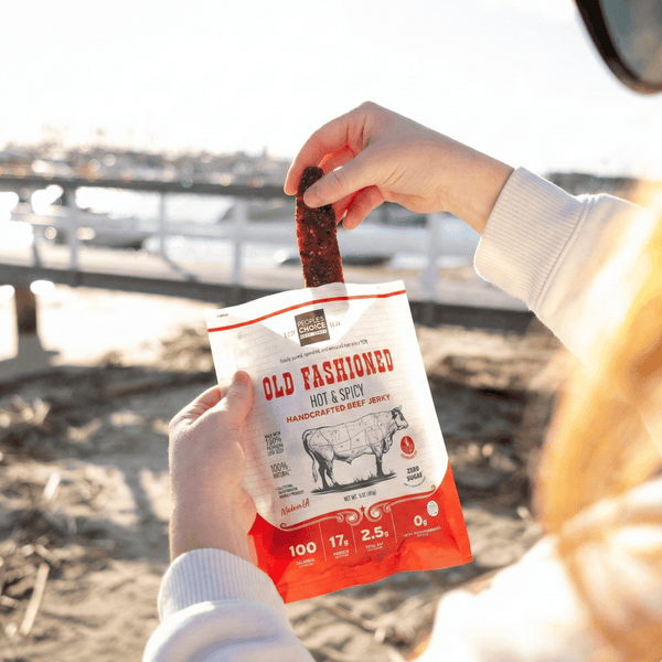 Person holding a bag of 'Old Fashioned' hot and spicy beef jerky by a dock on a beach.