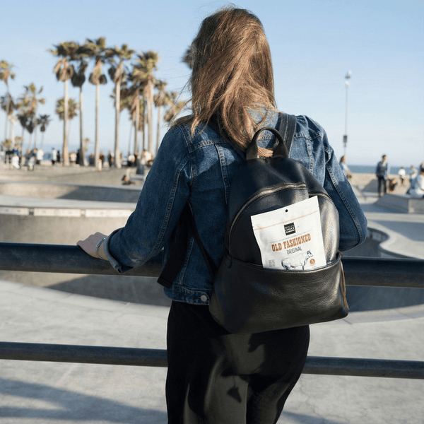 Woman standing outside a skating park wearing a black backpack with a package of beef jerky in it 