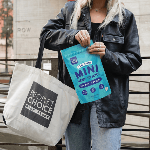 Person holding a bag of People's Choice beef jerky with a tote bag.