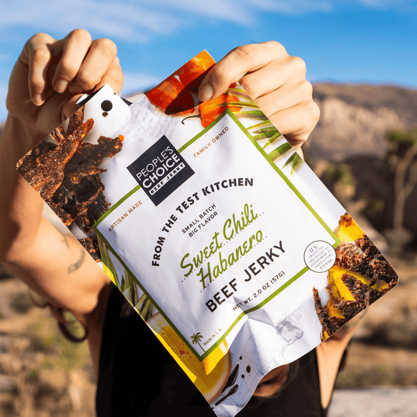 Person holding a package of Sweet Chili Habanero Beef Jerky with a desert landscape in the background