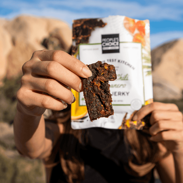 Person holding a package of People's Choice beef jerky with a mountainous background