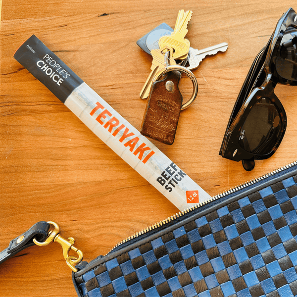Teriyaki beef stick on a table next to a purse and keys and sunglasses. 