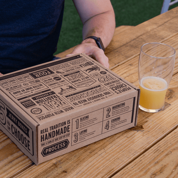 Branded beef jerky box on a wooden table next to a beer. 