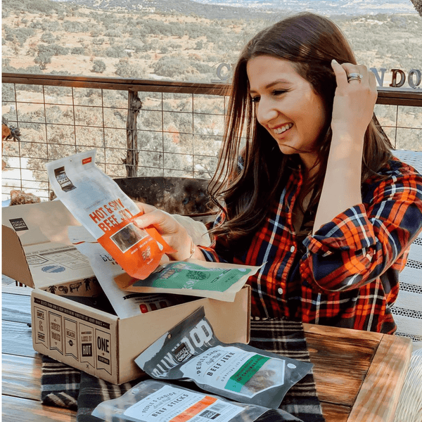 A smiling woman looking at a beef jerky box. 