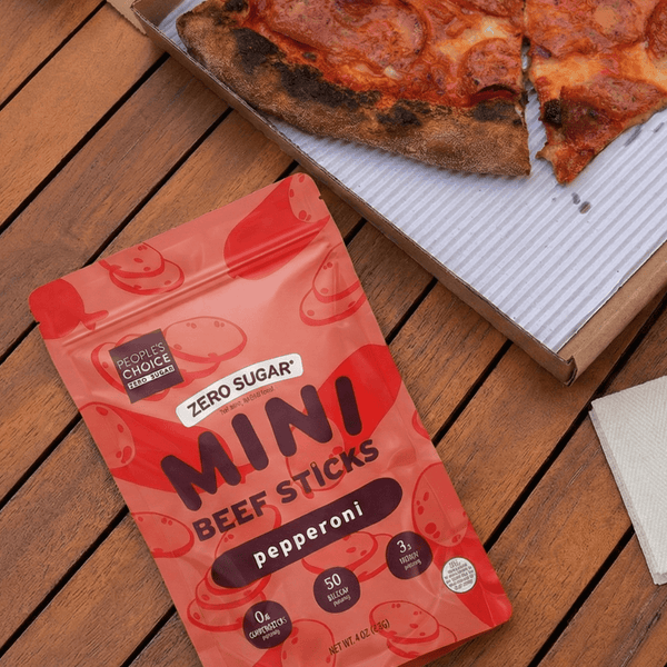 Pepperoni Mini Beef Sticks on a wooden table with a pizza in the background