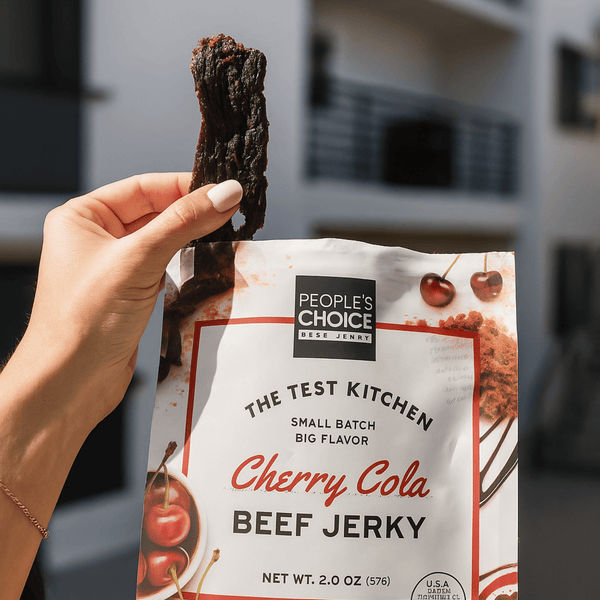Hand holding a piece of cherry cola beef jerky in front of its packaging.