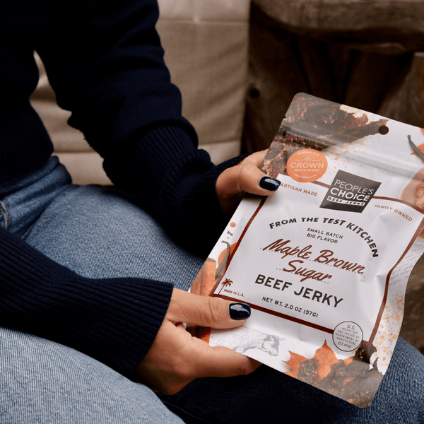 Person holding a package of Maple Brown Sugar Beef Jerky in a rustic setting.