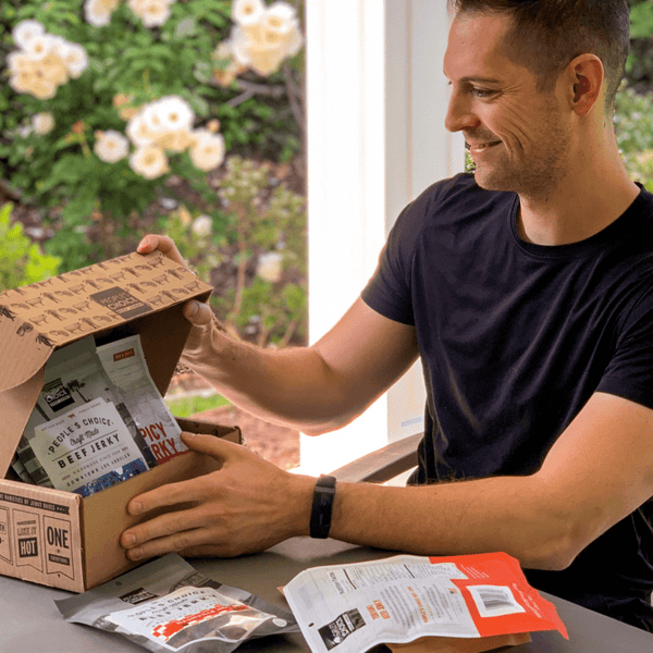 Man smiling while looking at a beef jerky box outside at a table. 