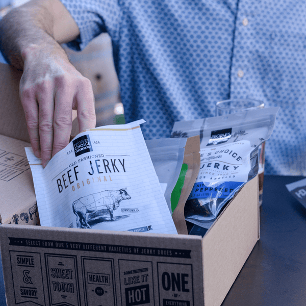 Man reaching into a bag of beef jerky that's in a jerky box at a table. 