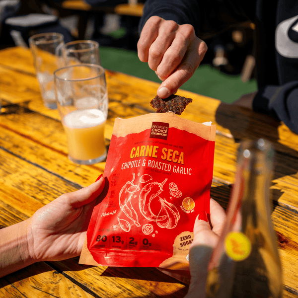 Two friends sharing a bag of Carne Seca Chipotle and Roasted Garlic at a picnic bench at a brewery