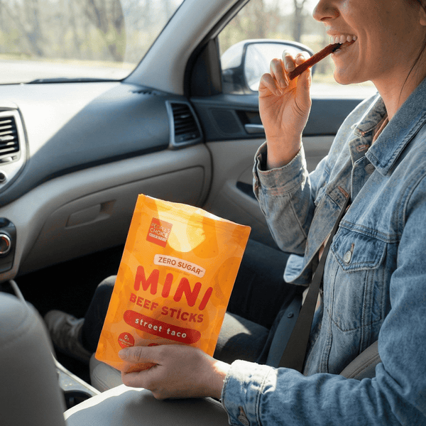 Person sitting in a car holding a package of mini beef sticks.