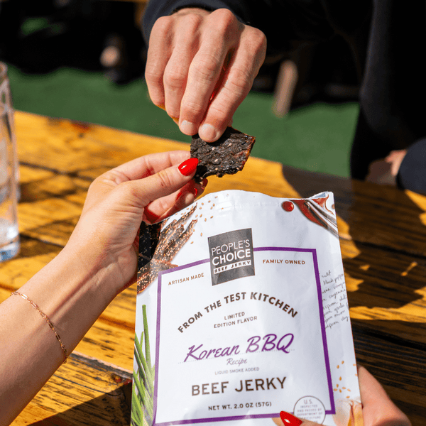 Two people sharing a bag of Korean BBQ beef jerky while sitting at a picnic table